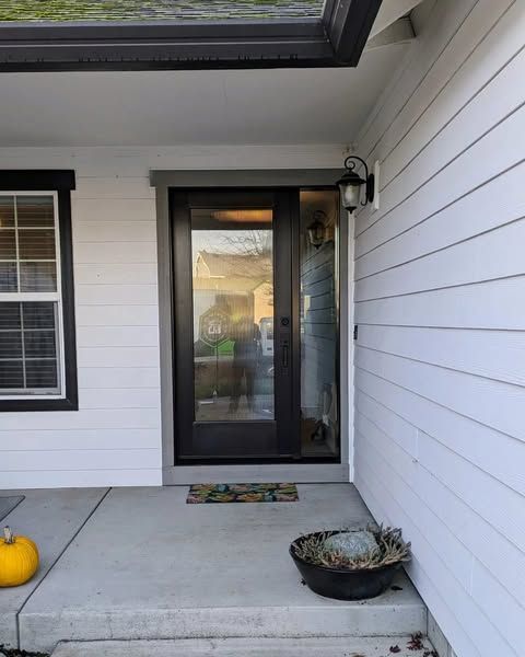 Front door of a house with black frame, glass, and a small porch. White siding and a pumpkin are on the left.