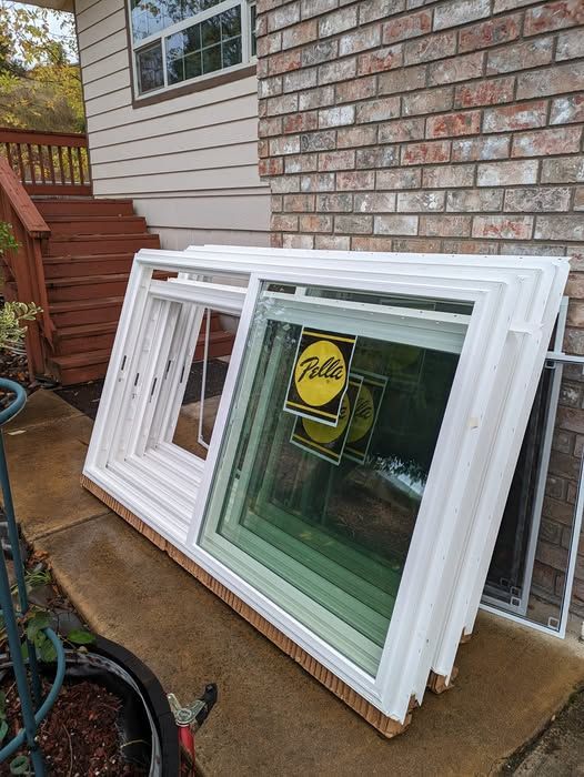 White-framed windows stacked against a brick wall, some with glass, and a sticker.  Outdoor setting, daylight.