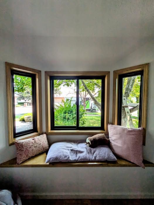 Bay window with a built-in bench, pillows, and view of trees and a house.