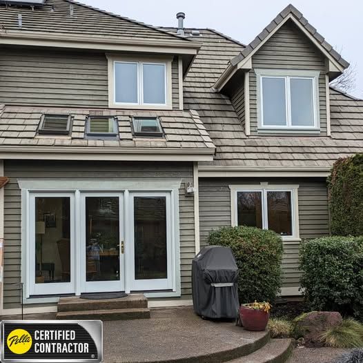 Exterior of a two-story house with green siding, white-framed windows, and a gray shingled roof.