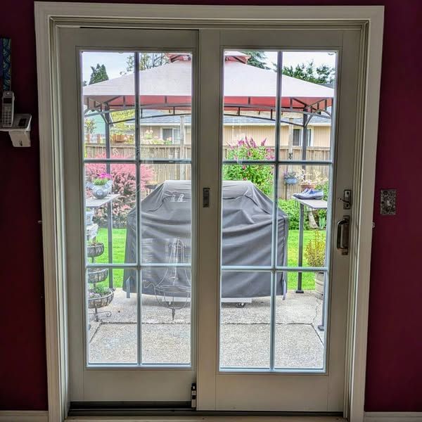 White-framed glass patio doors open to a backyard with a covered grill, gazebo, and flowers.