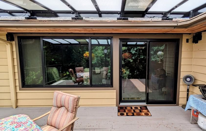 Sliding glass doors and windows on an outdoor deck, framed in black. An awning is above.