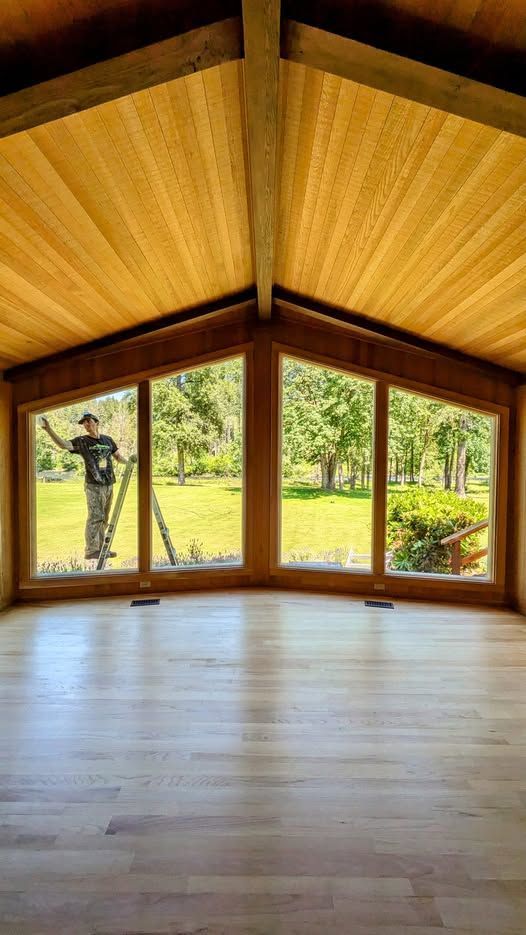 Empty room with large windows overlooking a green yard; a person on a ladder cleans the window.