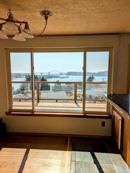 Dining room with large window overlooking a bridge and ocean. Brown cabinets and flooring, blue sky.