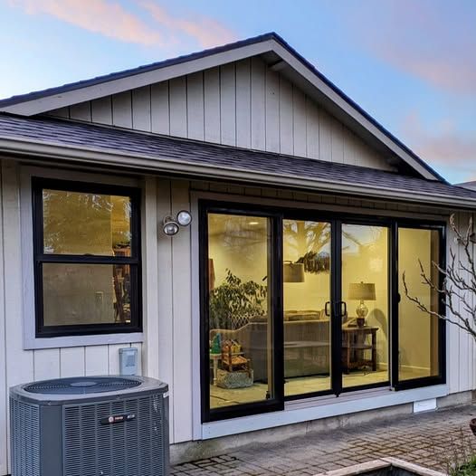 Exterior of a house with sliding glass doors and a window. An AC unit sits on the ground near the house.