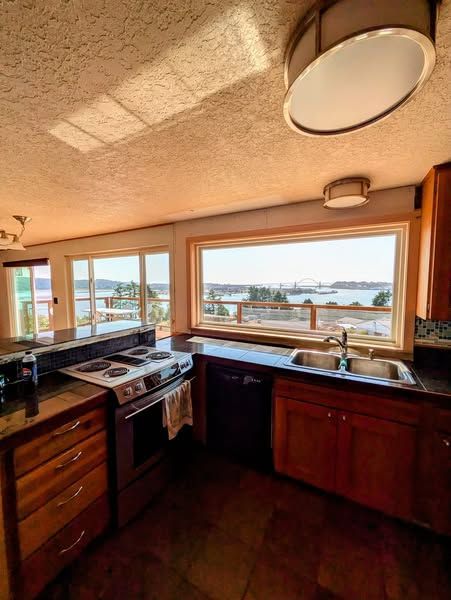 Kitchen with large window overlooking a body of water. Wooden cabinets, stove, and sink.