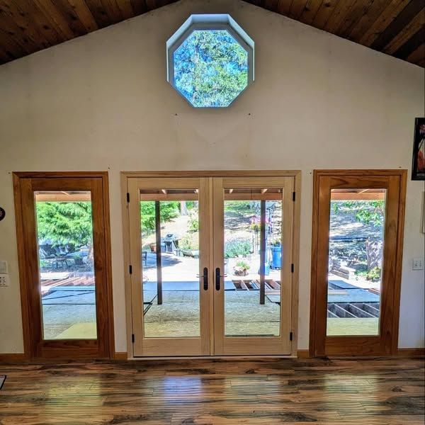 Wooden doors and windows in a room with a high ceiling, and an octagonal window looking outside.