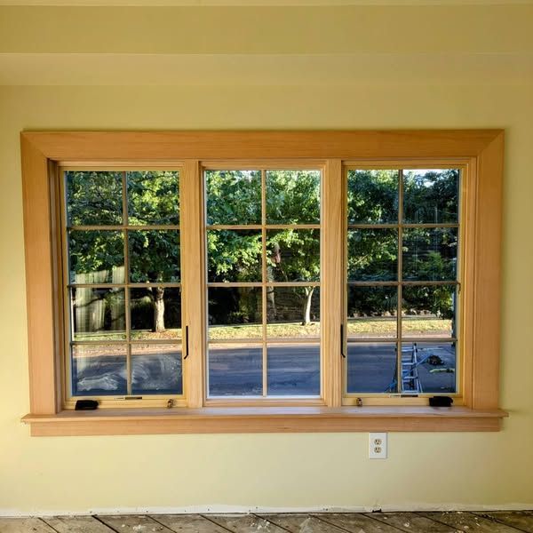Triple window with wood trim, overlooking trees and street.