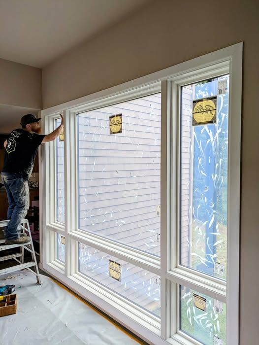 Person on a stepladder installing white window trim in a room with neutral walls.