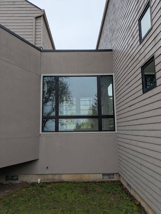 Exterior of a building with a large window; gray stucco and siding.