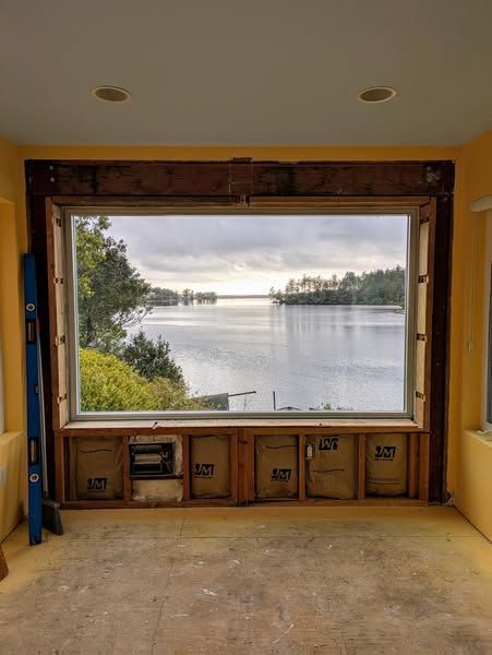 Interior room with large window overlooking a body of water. Construction in progress; yellow walls.
