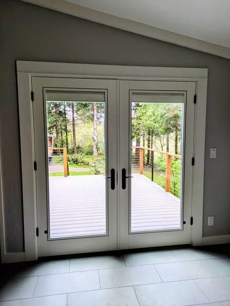 White French doors with glass panes, framed in white trim, opening to a wooden deck with a forest view.