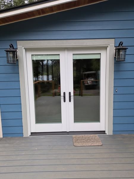 White double doors with glass panels and black handles. Blue siding, gray trim, and outdoor lights.
