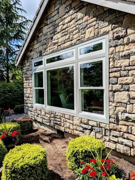 Stone house exterior with white-framed windows, and landscaping.