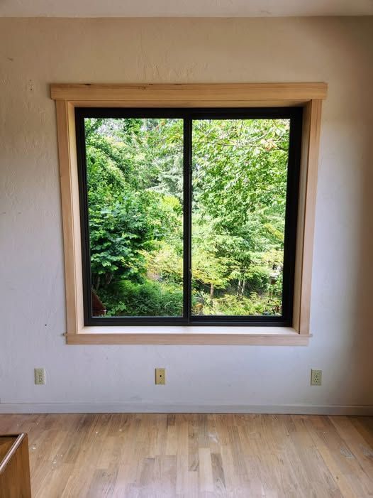 Window with dark frame and light wood trim, overlooking lush green trees.