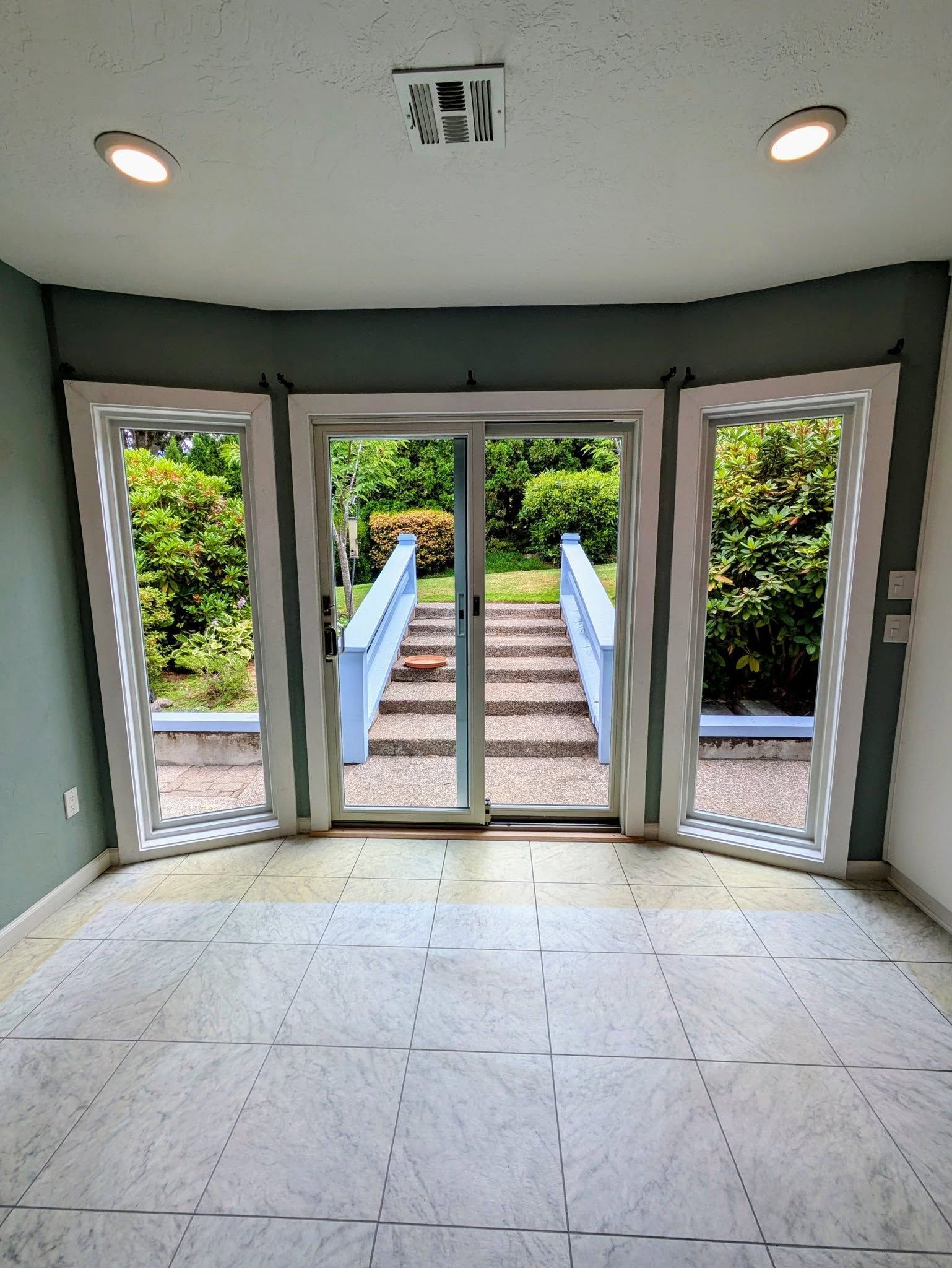 Interior room with large windows overlooking outdoor stairs leading to a green yard.