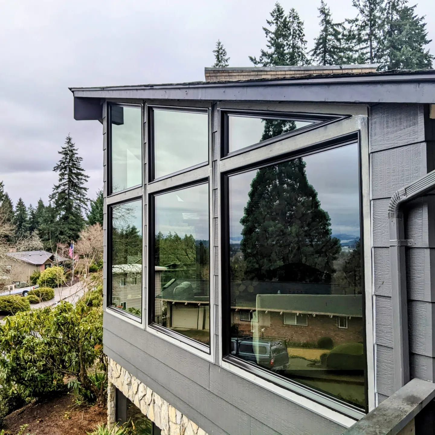 Exterior of a house with large windows overlooking a green landscape on a cloudy day.