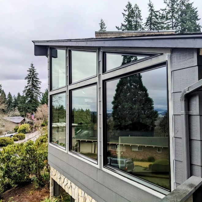 Exterior of a house with large windows overlooking a green landscape on a cloudy day.