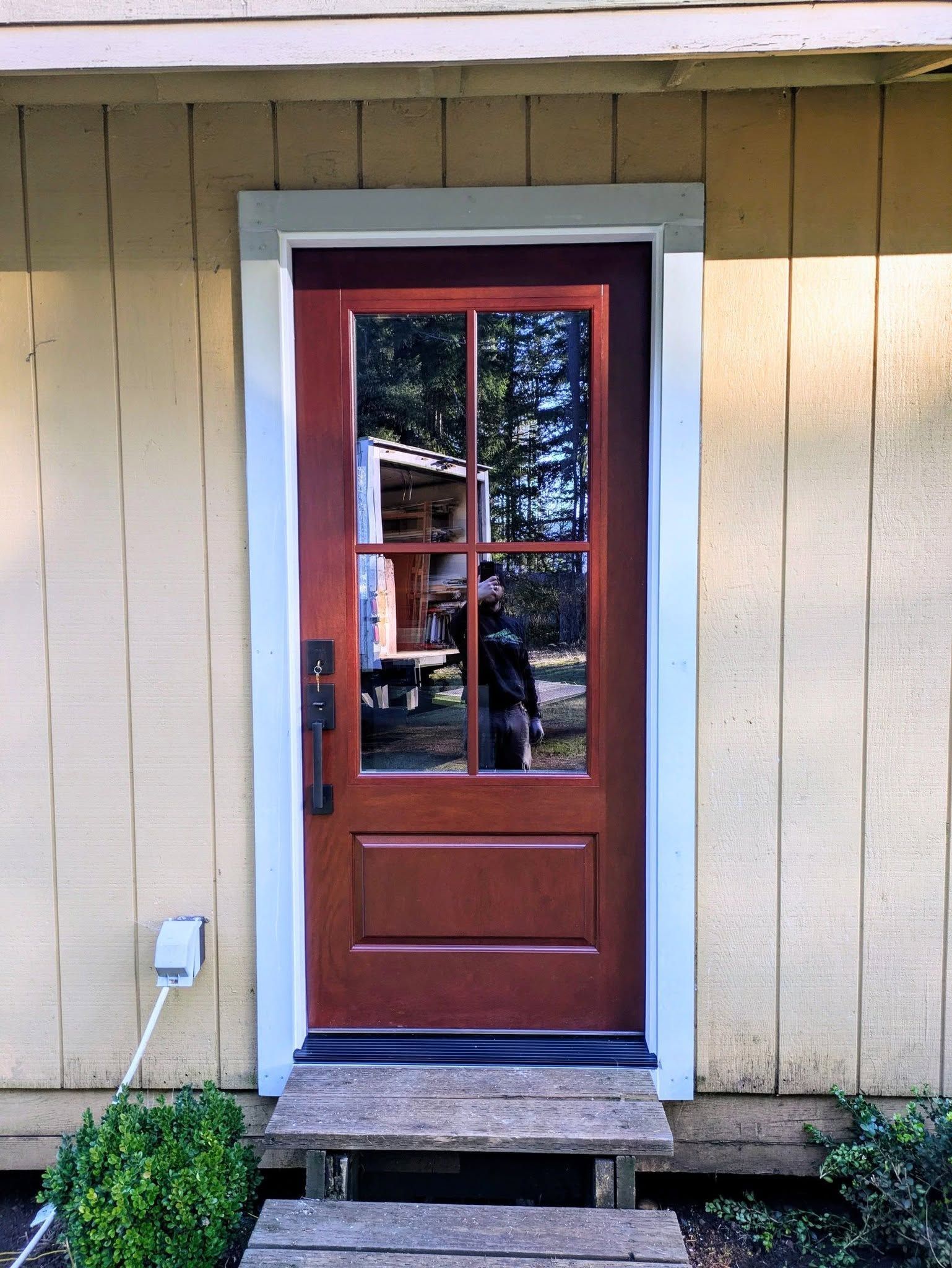 Red front door with glass panels, white trim, and small wooden steps.