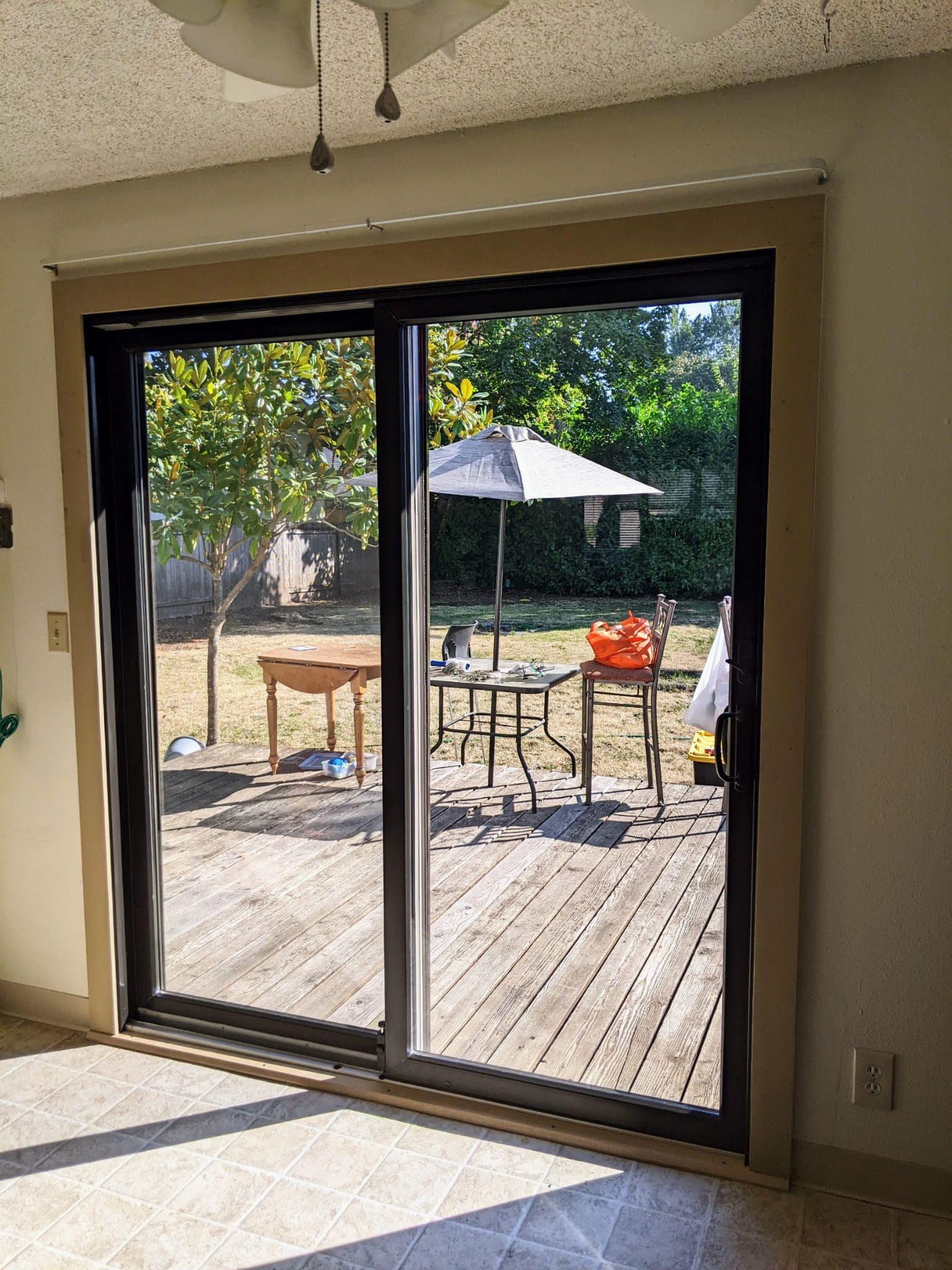 Sliding glass door leading to a backyard deck with patio furniture and umbrella; sunny outdoor view.