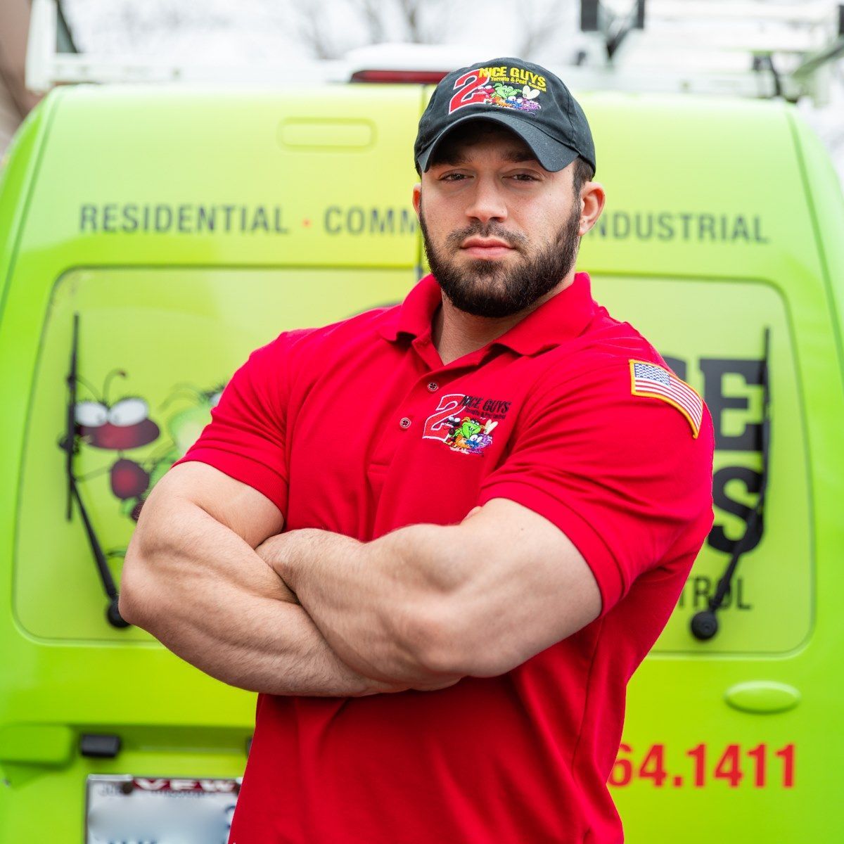 Man in red polo and hat with arms crossed in front of a green pest control van.