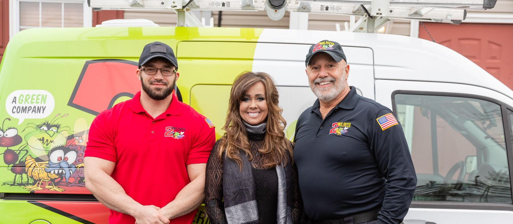 Three people stand in front of a green van. The van has cartoon graphics and the name 
