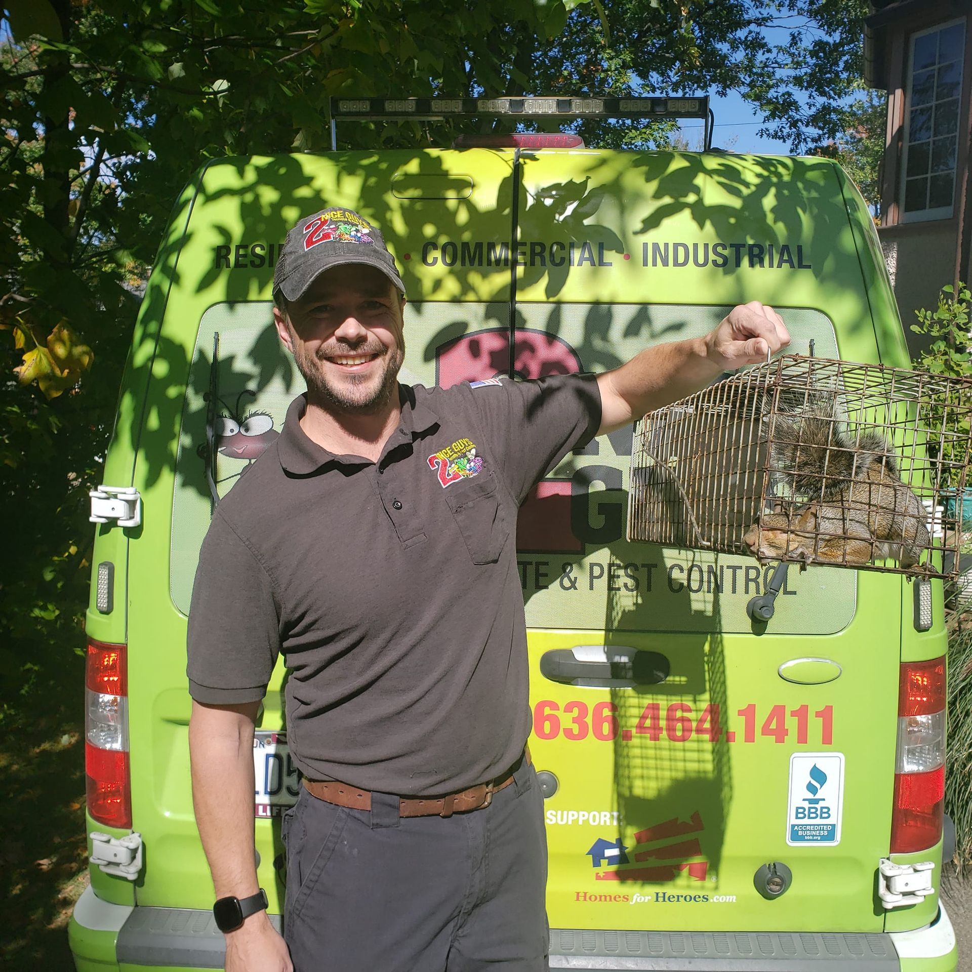 Man in front of green van holding animal cage, likely for pest control.