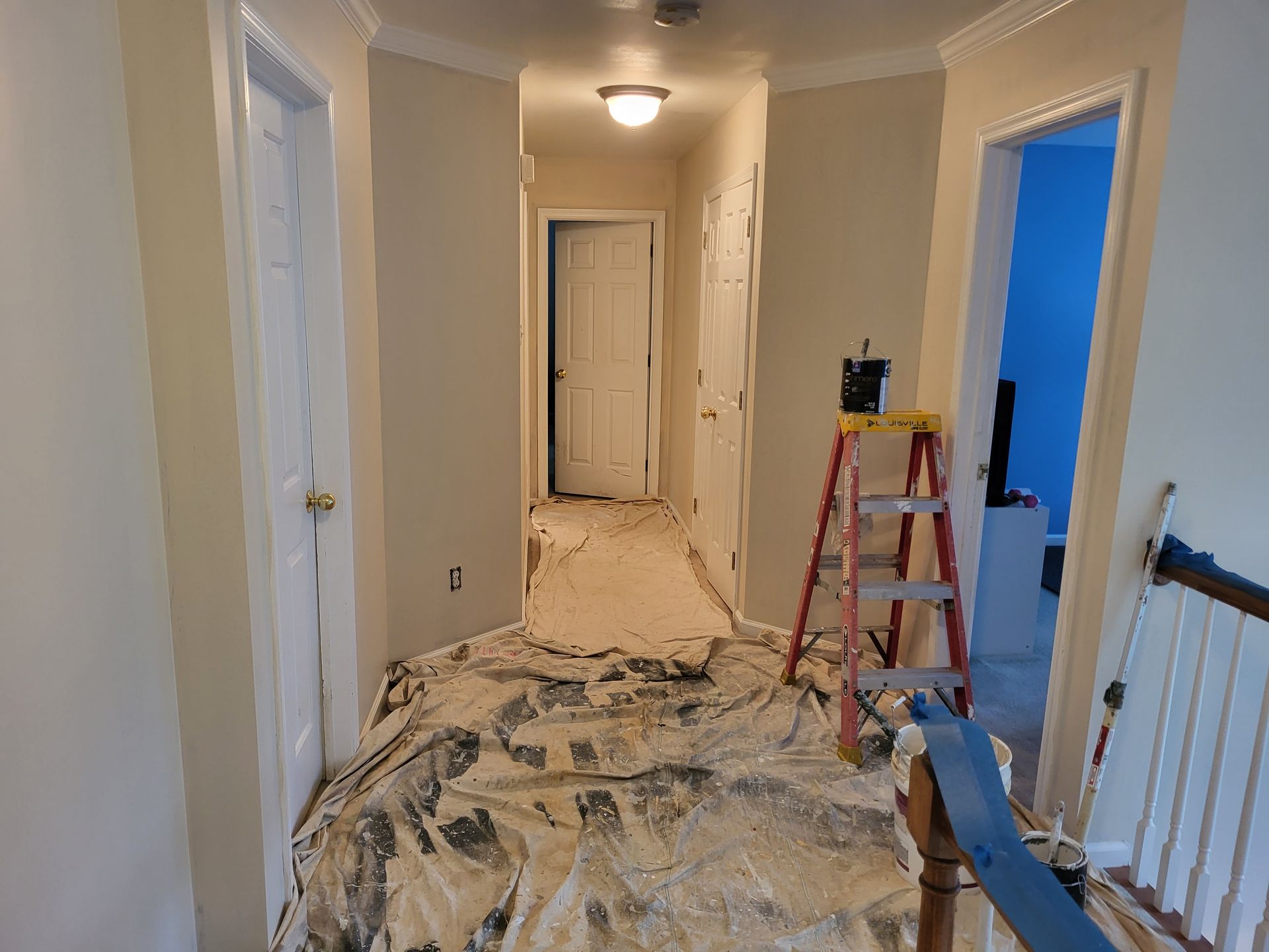 A hallway with a ladder and a tarp on the floor.