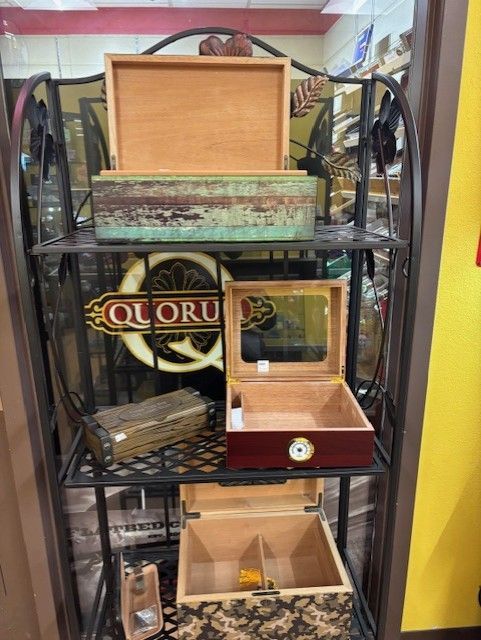 A metal shelf displays several open cigar boxes with various colors and textures against a blurred background.