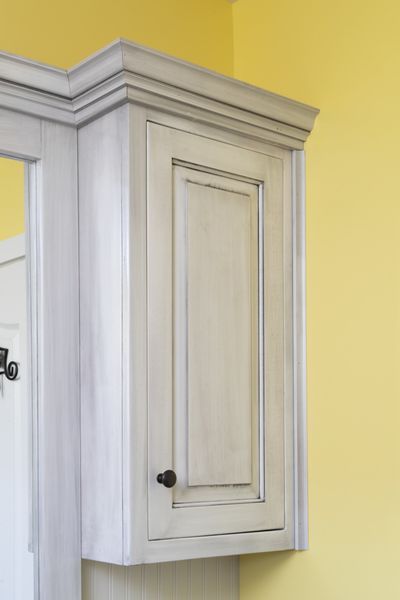 A white cabinet is hanging on a yellow wall