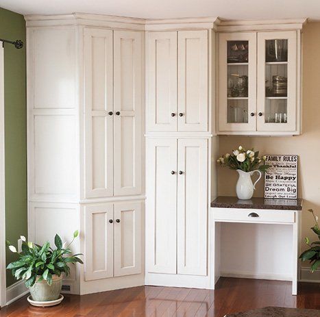 A corner of a room with white cabinets and a desk