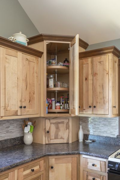 A kitchen with wooden cabinets and a pantry with the door open.
