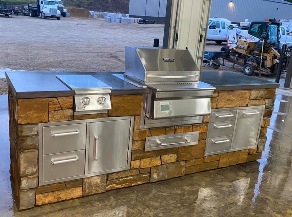 A large outdoor kitchen with stainless steel appliances and brick walls.