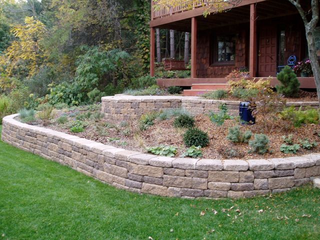 A stone wall surrounds a lush green lawn in front of a house.