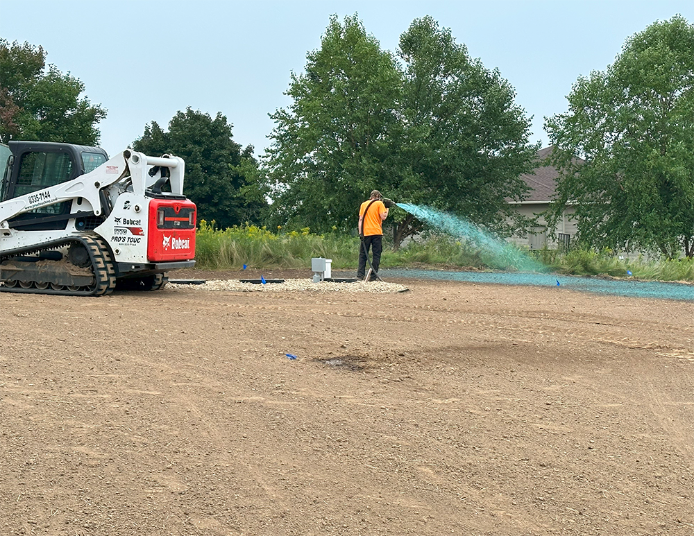 A man is standing in front of a bulldozer spraying water on a dirt field.