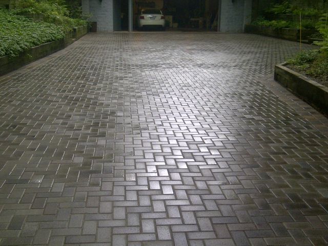 A brick driveway leads to a garage with a car parked in it.