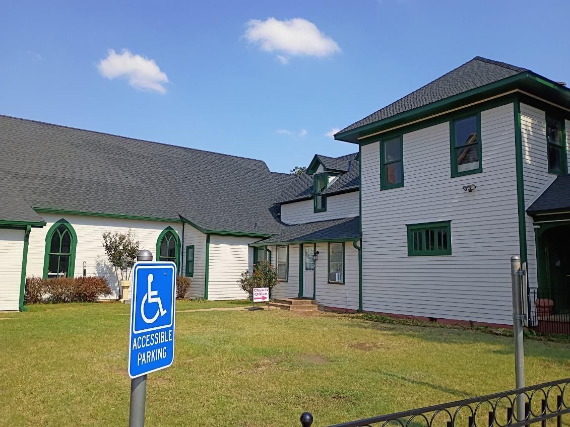Accessible parking sign in front of a white building with green trim and a dark roof under a blue sky