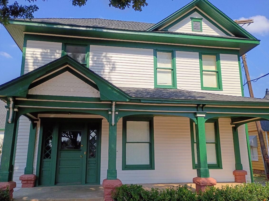 Green-trimmed white house with a front porch and gabled roof under a clear blue sky