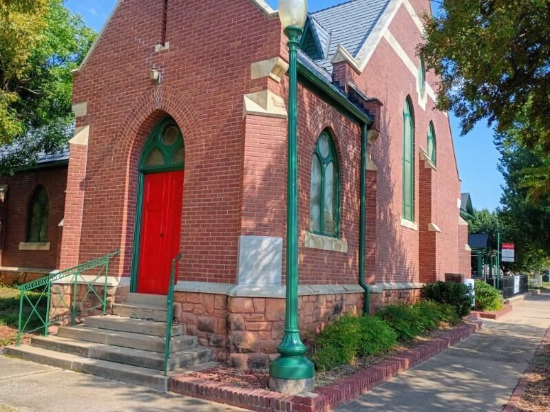 Red brick church corner with arched red door, green trim, and a green lamppost beside steps
