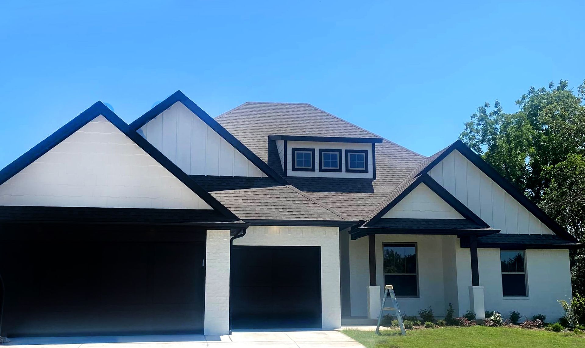 Modern white house with black garage doors and dark roof trim under a clear blue sky