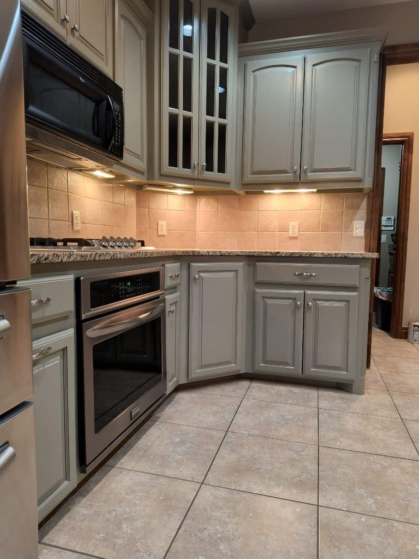 Modern kitchen with gray cabinets, stainless steel appliances, beige tile backsplash, and tiled floor.