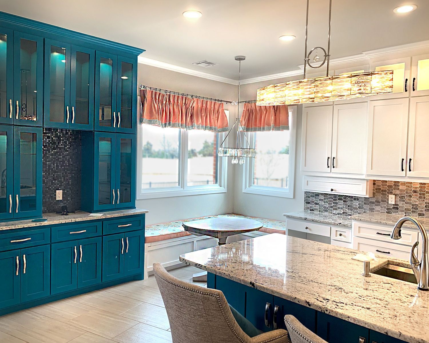 Bright kitchen with teal cabinets, white marble countertops, and a large island by sunlit windows.