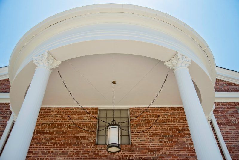 Brick building with white columns and arched roof, hanging light, bright blue sky.
