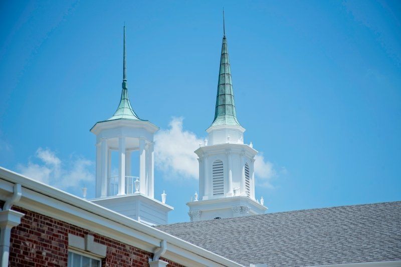 Two white church steeples with green accents against a blue sky, viewed from a building's roof.