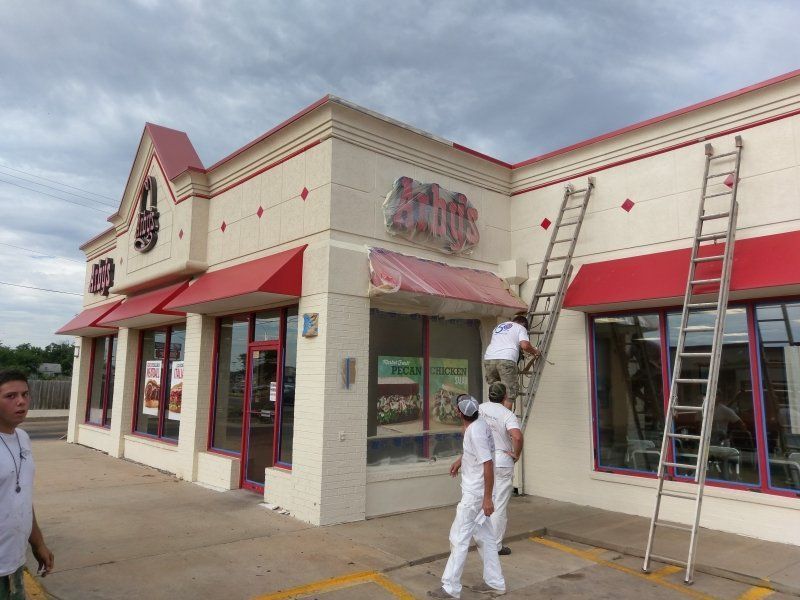 Exterior of a restaurant being painted by workers on ladders; red accents, cream walls.