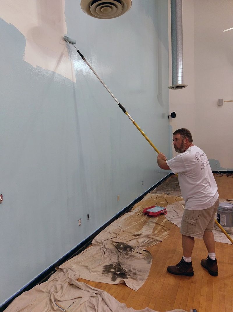 Person painting a tall wall light blue with a roller on an extension pole.