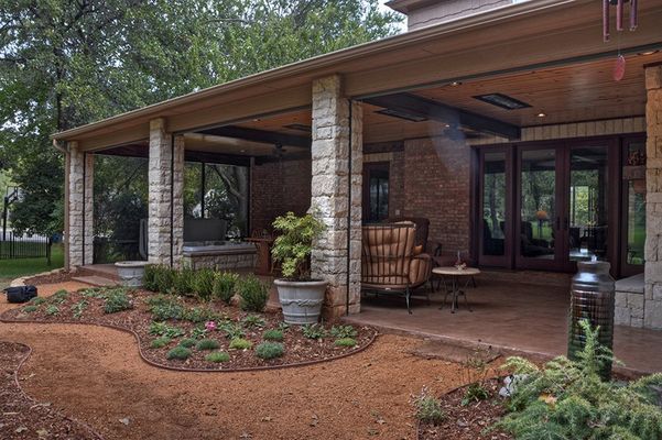 Covered outdoor patio with a seating area, landscaping, and tall stone columns.