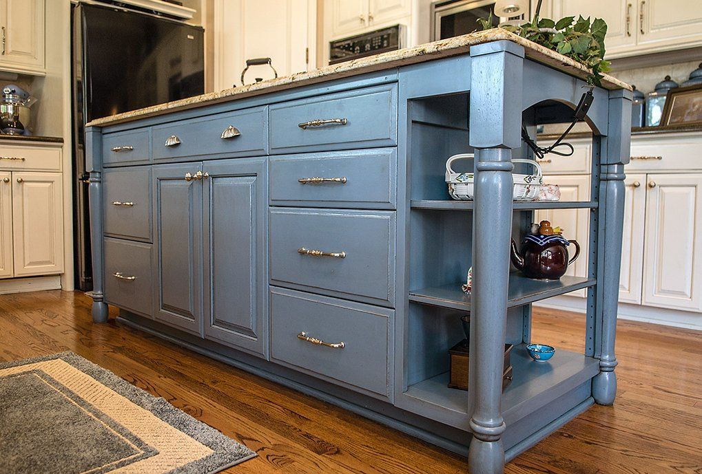 Blue kitchen island with drawers, cabinets, and shelves; wooden countertop, set on a hardwood floor.