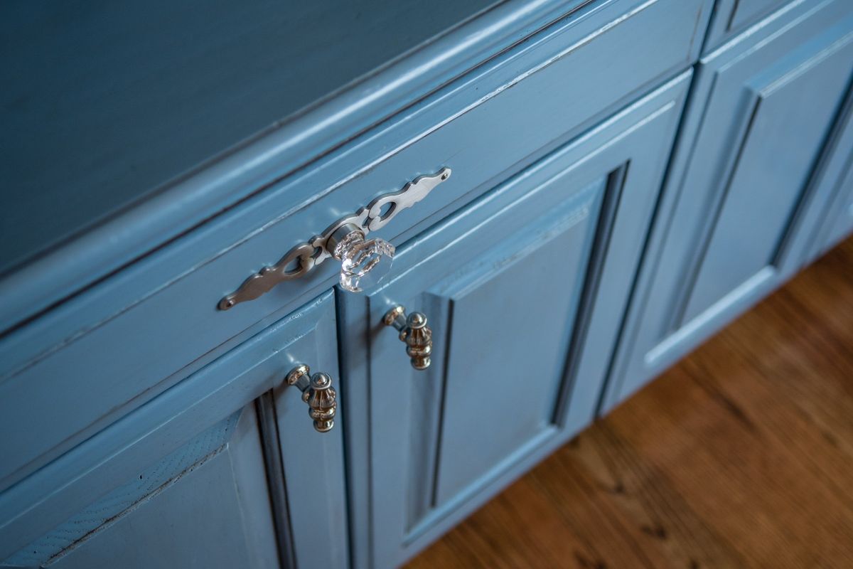 Blue kitchen cabinets with ornate crystal-like knobs. Wooden floor in foreground.