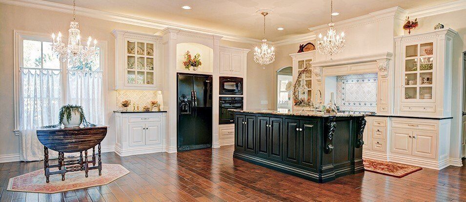 A luxurious kitchen with a black island, white cabinets, and crystal chandeliers.